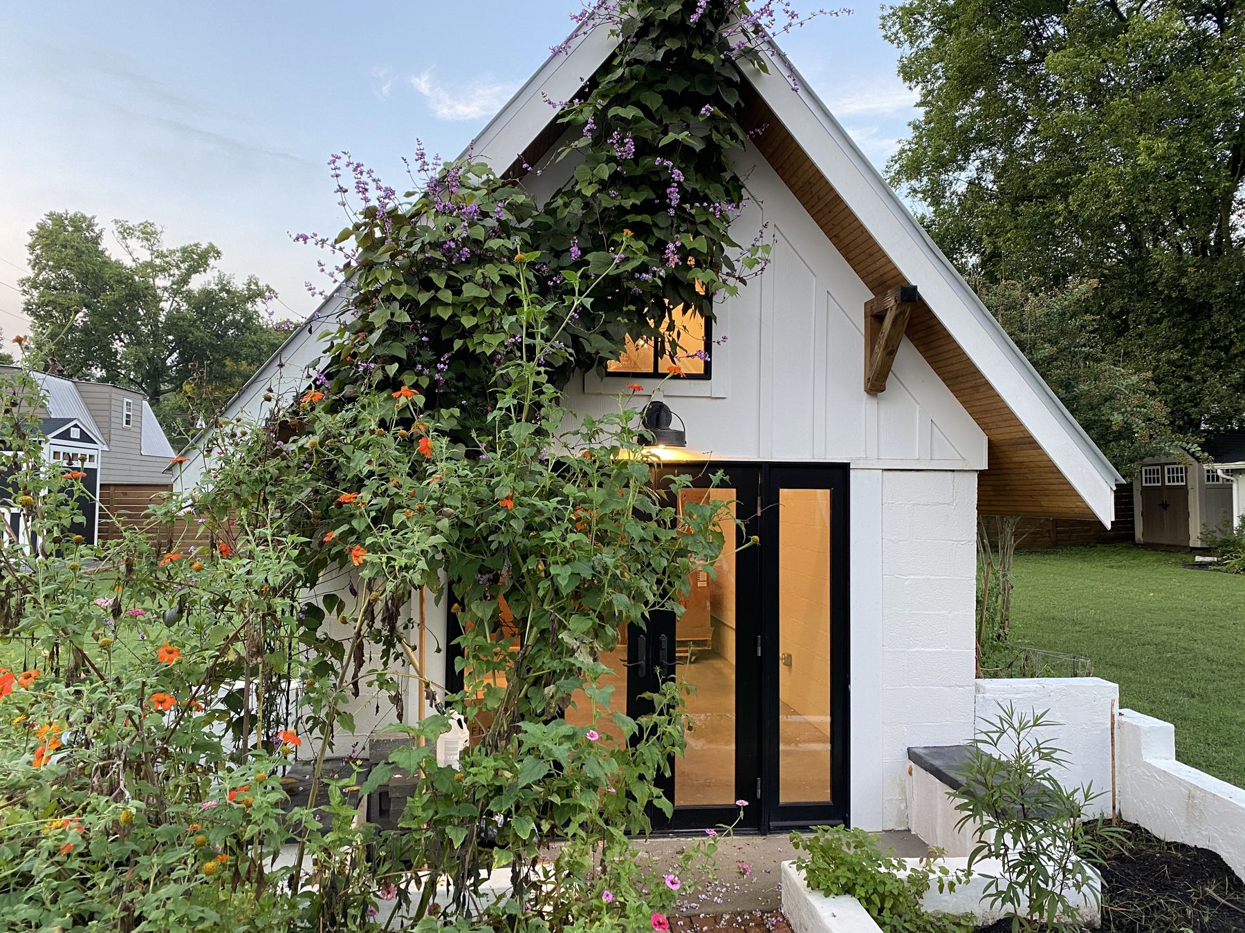 The white gabled Kirkegaard house at dusk, with flowering vines and zinnias by the front doors